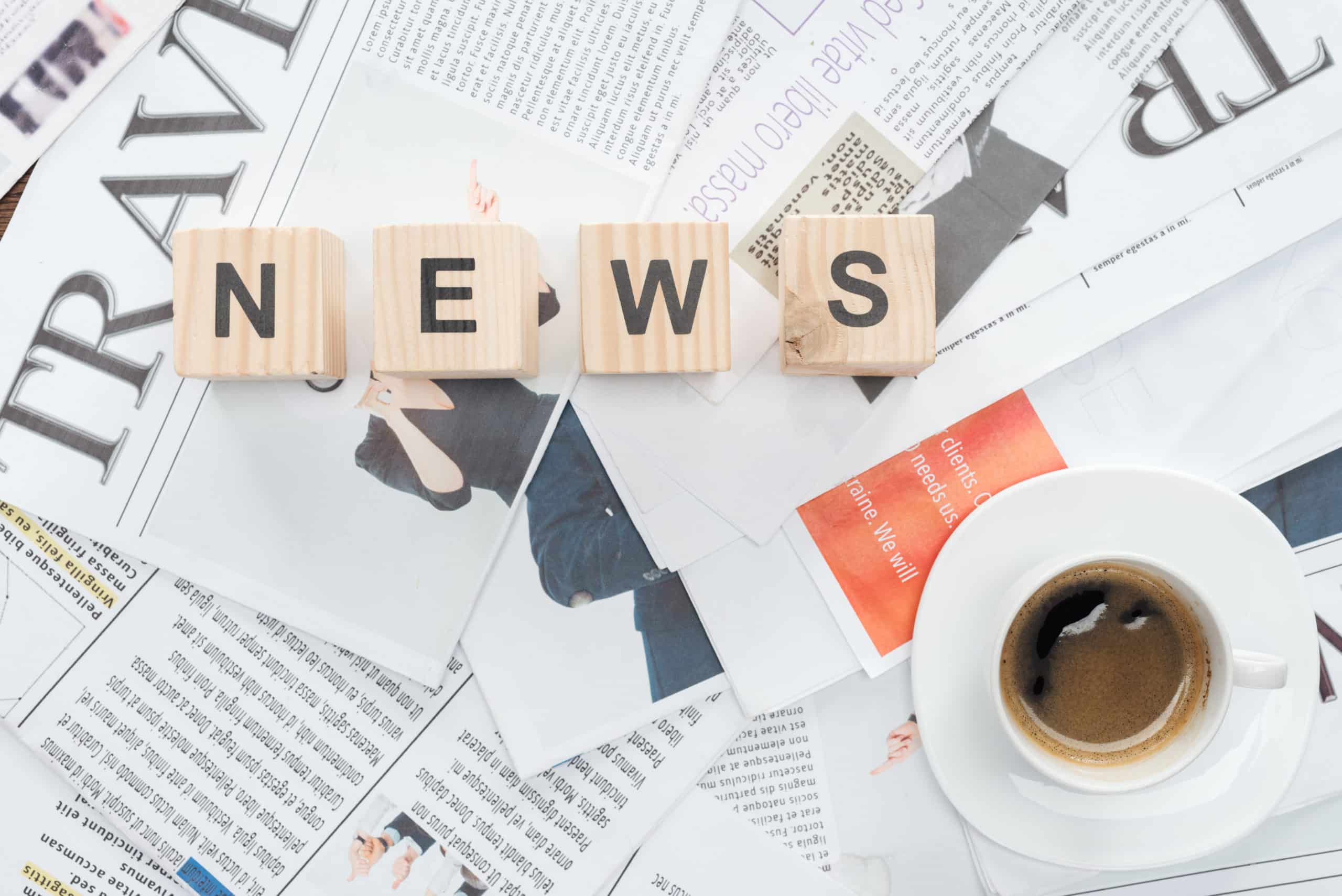 top view of wooden cubes with word news and cup of coffee on newspapers