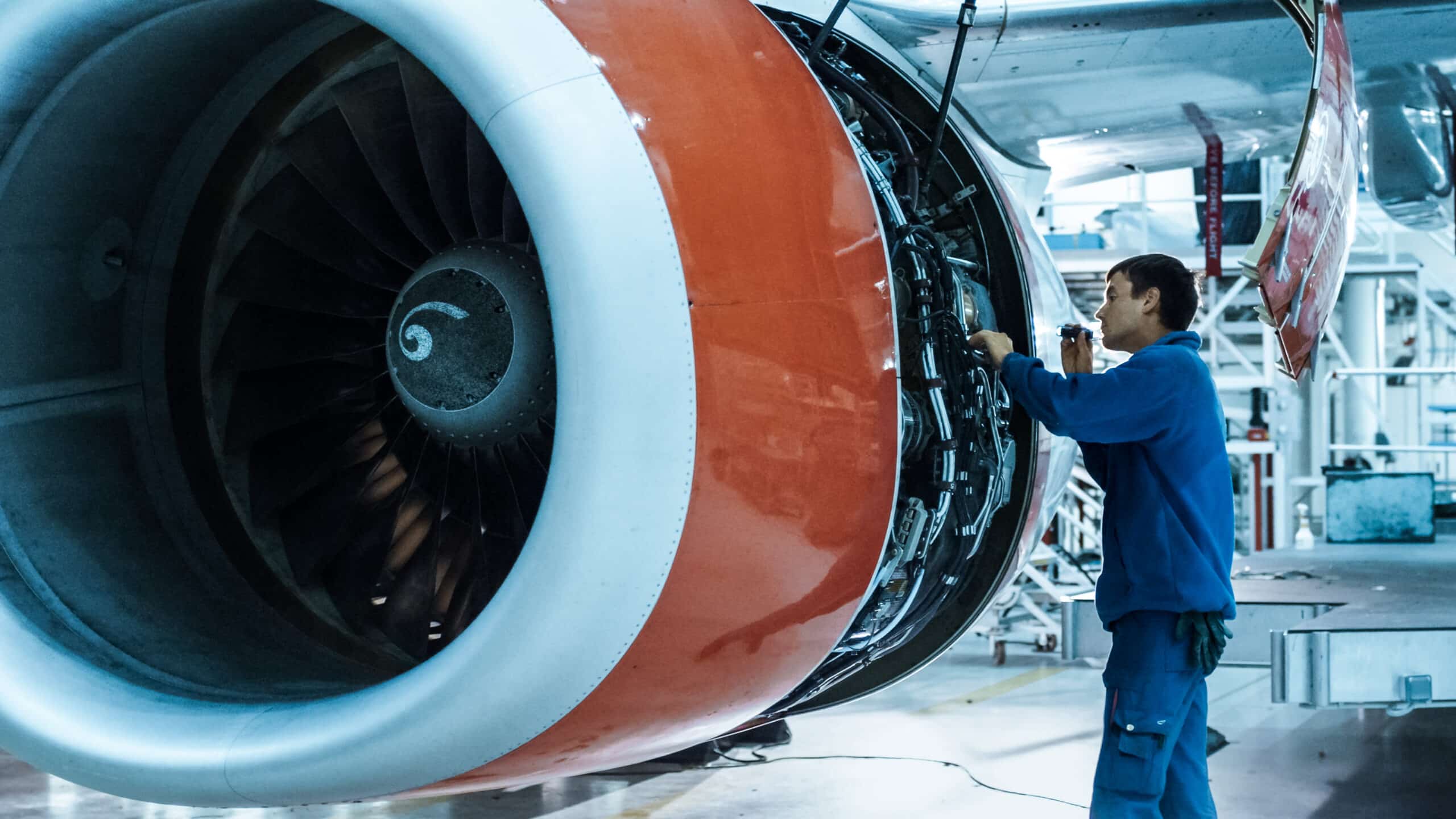 Aircraft maintenance mechanic with a flash light inspects plane engine in a hangar. a man manually performing a visual inspection on an airplane engine