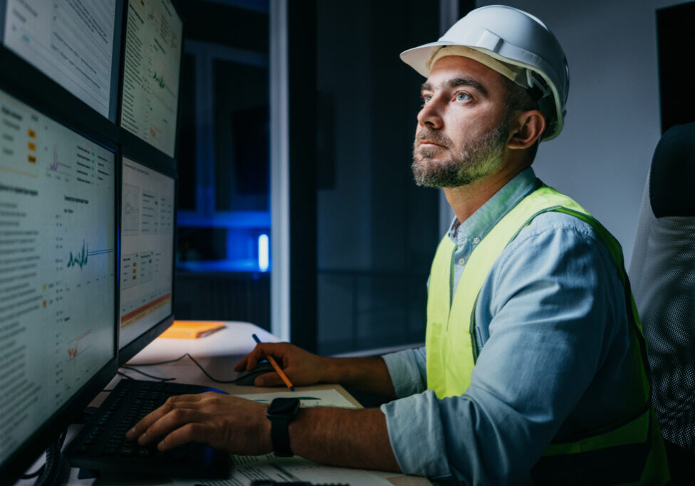 Bearded operator of factory control industry process using monitors. Engineer follow on production line